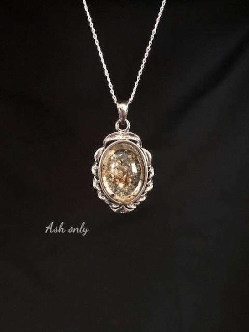 May include: A silver chain necklace with a silver oval pendant. The pendant has a clear glass insert filled with ash.