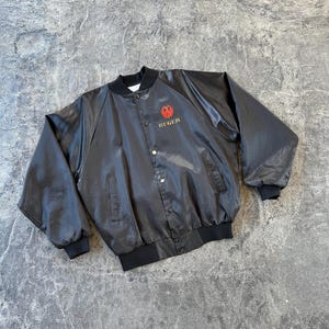 May include: A black satin bomber jacket with a red and gold Ruger logo on the left chest.