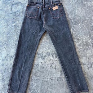 May include: A pair of dark wash denim jeans with red stitching detail and a leather patch with the Wrangler logo on the back.