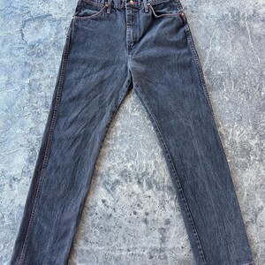 May include: A pair of dark wash denim jeans with a straight leg fit. The jeans have red stitching detail around the pockets and seams.
