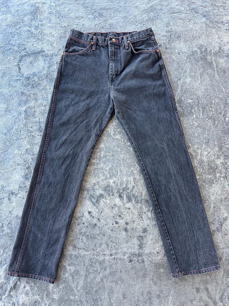 May include: A pair of dark wash denim jeans with a straight leg fit. The jeans have red stitching detail around the pockets and seams.