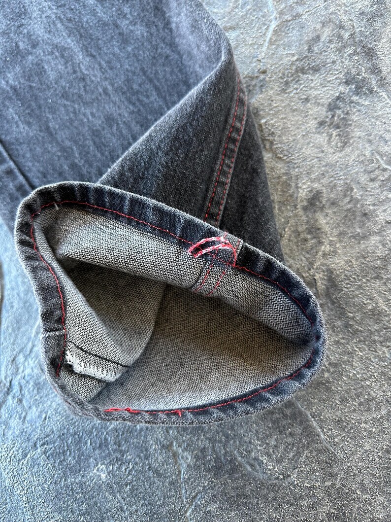 May include: Close-up of the inside of a pair of dark grey denim jeans with red stitching. The jeans are folded over to show the inside of the fabric.