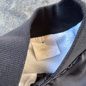 May include: A black satin bomber jacket with a ribbed collar and a white tag that reads "Manufactured in USA" and "L".