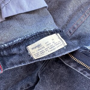 May include: A black pair of Wrangler jeans with a white tag that reads "Wrangler" and has the following information: "Style 13MWZRB, Waist 33, Length 34, Machine Wash Inside Out With Like Colours, Tumble Dry, Remove Promptly, Made in USA, R8HAF923 26WPL6428".