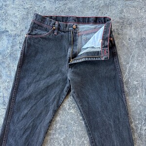 May include: A pair of dark wash denim jeans with a red stitch detail around the waistband and pockets.