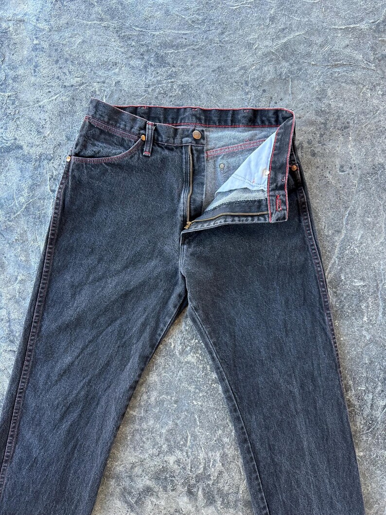 May include: A pair of dark wash denim jeans with a red stitch detail around the waistband and pockets.