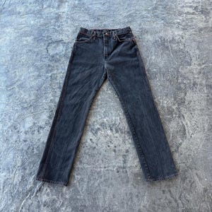 May include: A pair of dark wash denim jeans with red stitching detail. The jeans have a straight leg and a classic five-pocket style.