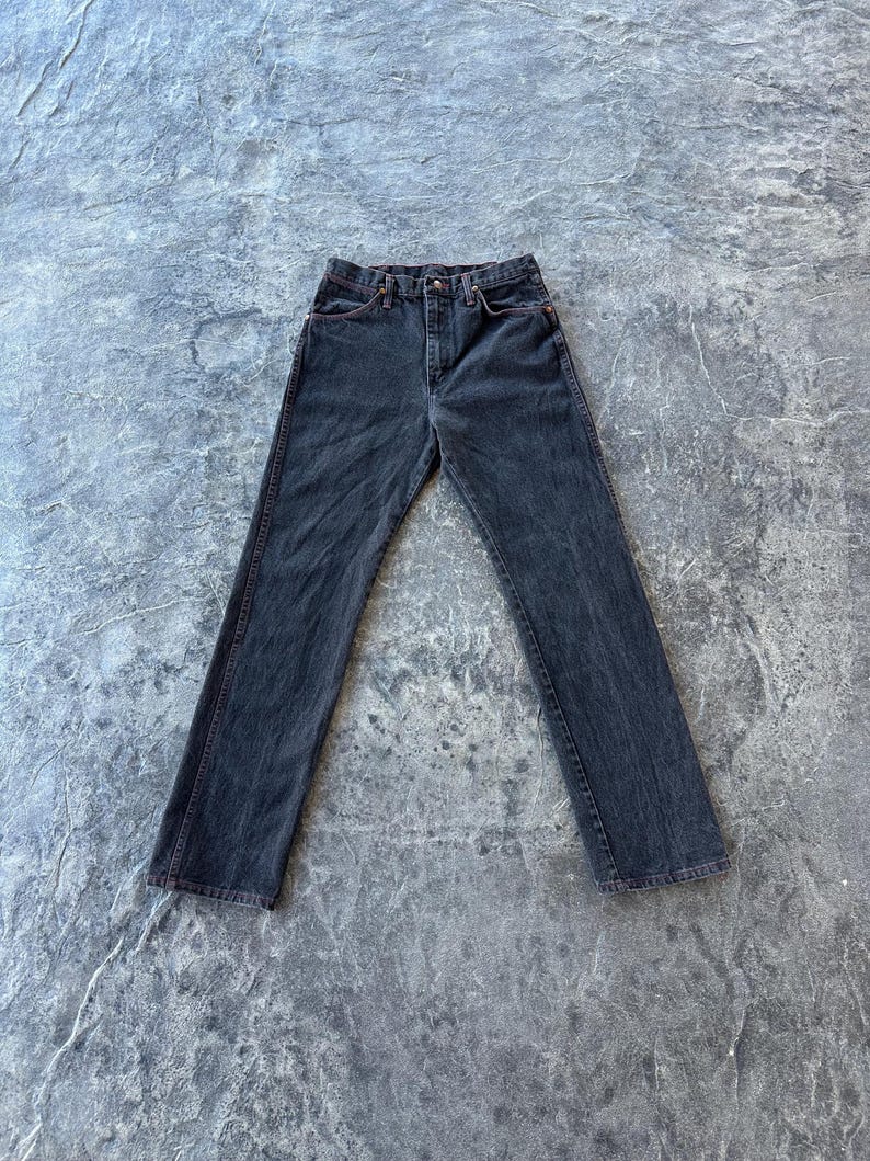 May include: A pair of dark wash denim jeans with red stitching detail. The jeans have a straight leg and a classic five-pocket style.