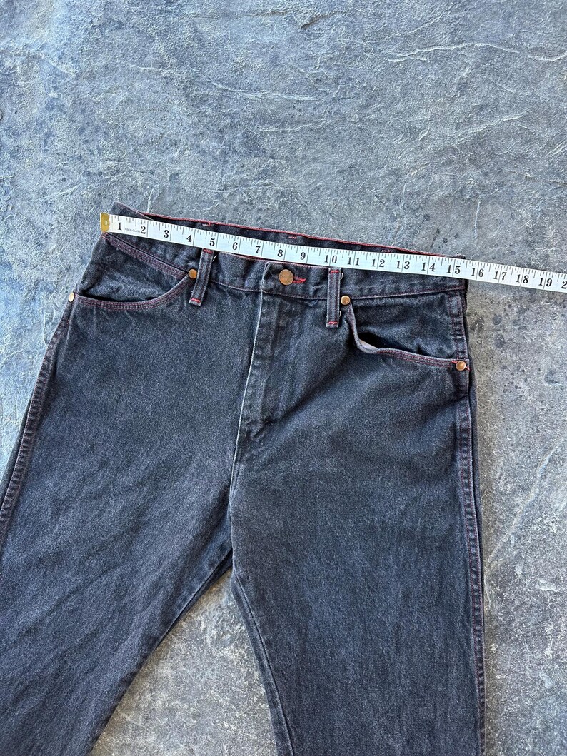 May include: A pair of dark wash denim jeans with red stitching. The jeans have a straight leg and a classic five-pocket style.