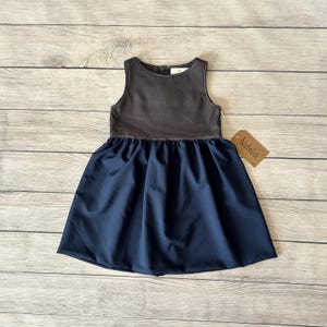 May include: A sleeveless dress with a dark gray top and a navy blue skirt. The dress has a gathered skirt and a fitted bodice. The dress has a tag that says "Natalia".