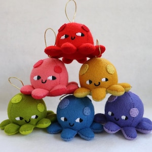 May include: A stack of six colorful plush octopus ornaments. The ornaments are in shades of red, pink, yellow, green, blue, and purple. Each octopus has a smiling face with white eyes and a gold string for hanging. These handmade ornaments are perfect for adding a touch of whimsy to any space.