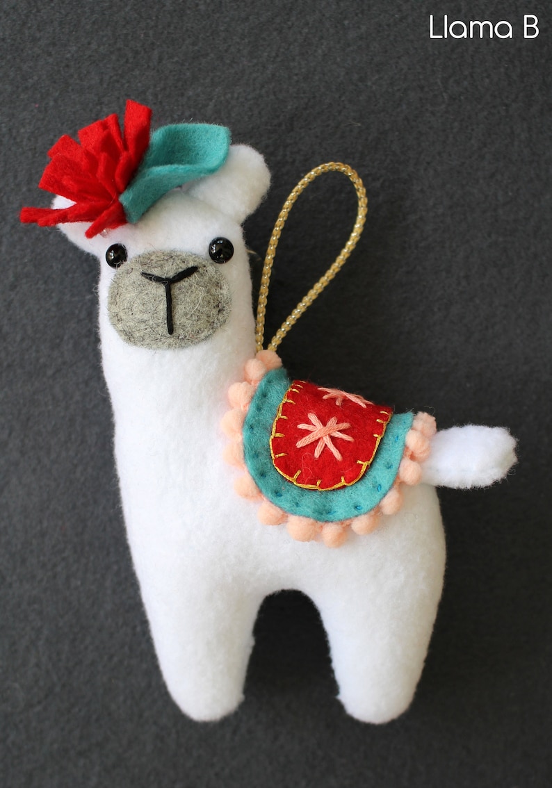 May include: White felt llama ornament with a red felt flower, teal felt hat, and a red and teal felt saddle with a pink pom-pom trim.