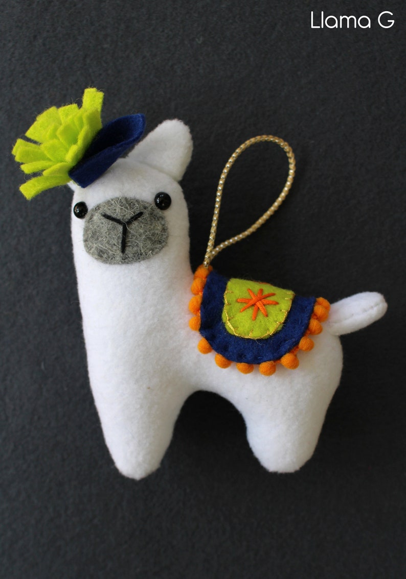 May include: White felt llama ornament with a green felt flower on its head, a blue felt hat, and a blue and green felt saddle with orange pom-poms.
