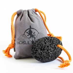 Puede incluir: Una bolsa de lona gris con un cordón de ajuste naranja y un logotipo de león negro. La bolsa contiene una piedra pómez negra.
