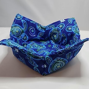 May include: A blue fabric bowl with a patterned design of green and white sea turtles. The bowl is folded and ready to be used.