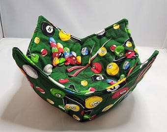 May include: Green fabric bowl with a pool table design featuring billiard balls, cues, and a rack. The bowl is made of quilted fabric and has a square shape.