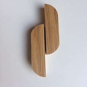 Puede incluir: Dos tiradores de armario de madera con acabado de vetas naturales. Cada tirador tiene forma rectangular con extremos redondeados, creando un dise&ntilde;o curvo. Los tiradores est&aacute;n colocados verticalmente sobre un fondo blanco.