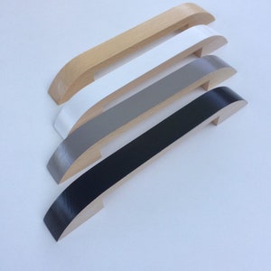 May include: Four wooden cabinet pulls in a row, each with a different color. The top pull is natural wood, followed by white, gray, and black. The pulls have a curved design and are made of wood.