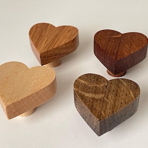 Può includere: Quattro pomelli per mobili in legno a forma di cuore, in varie tonalità di marrone e beige. Ogni pomello è montato su una piccola base rotonda in legno. La venatura del legno è visibile su ogni cuore.