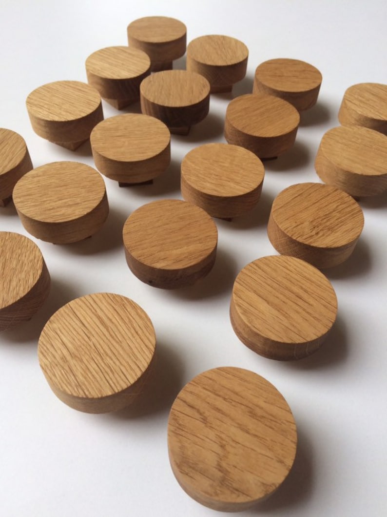 Puede incluir: Un conjunto de peque&ntilde;os pomos redondos de madera con un acabado de veta natural. Los pomos son de color marr&oacute;n claro y tienen forma cil&iacute;ndrica con una base ligeramente elevada. Est&aacute;n dispuestos sobre una superficie blanca.