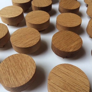 Puede incluir: Una colecci&oacute;n de peque&ntilde;os objetos redondos de madera con un acabado de veta natural. Los objetos son cil&iacute;ndricos con una parte superior e inferior planas. La madera tiene un color marr&oacute;n claro y c&aacute;lido. Los objetos est&aacute;n dispuestos sobre una superficie blanca.