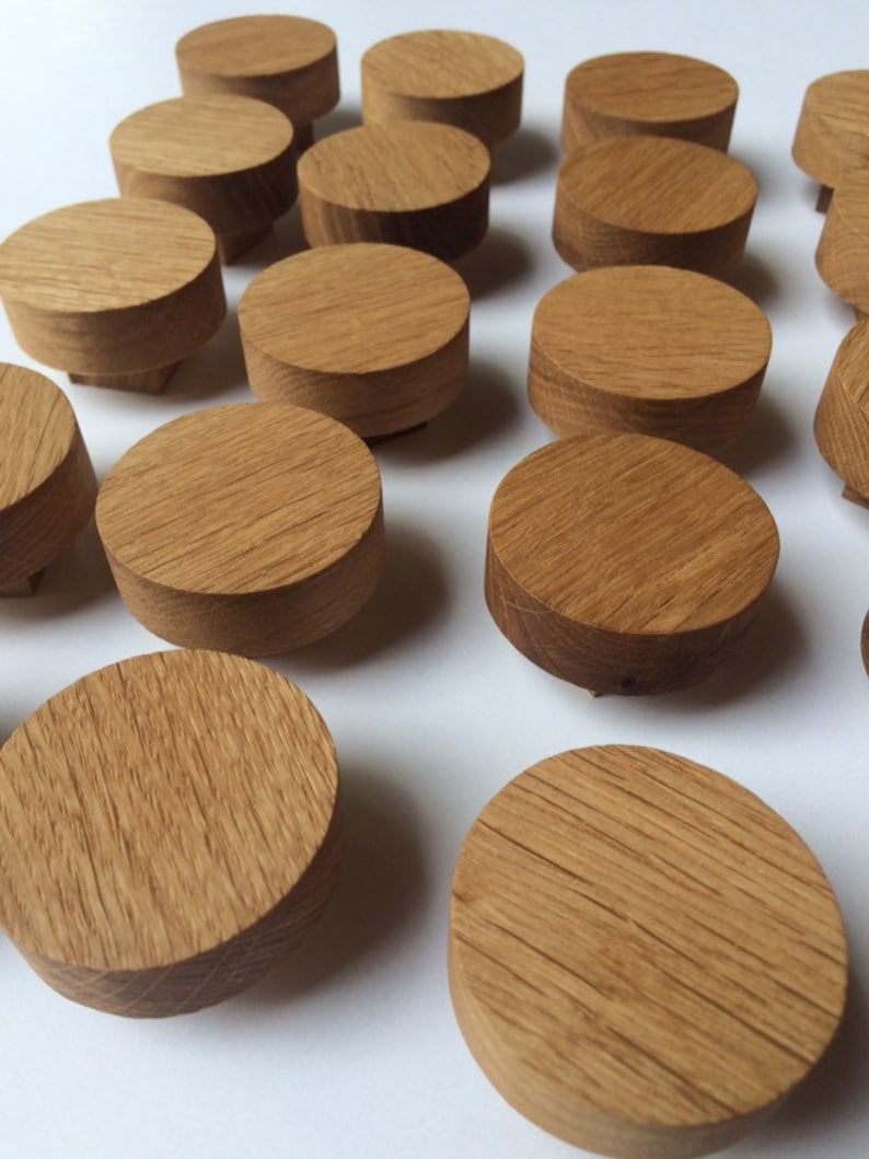 Puede incluir: Una colecci&oacute;n de peque&ntilde;os objetos redondos de madera con un acabado de veta natural. Los objetos son cil&iacute;ndricos con una parte superior e inferior planas. La madera tiene un color marr&oacute;n claro y c&aacute;lido. Los objetos est&aacute;n dispuestos sobre una superficie blanca.