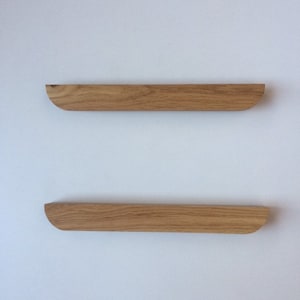 Puede incluir: Dos estantes flotantes de madera con acabado natural montados en una pared blanca. Cada estante es rectangular con un borde curvo en un lado. Los estantes son de madera marr&oacute;n claro y est&aacute;n alineados horizontalmente.