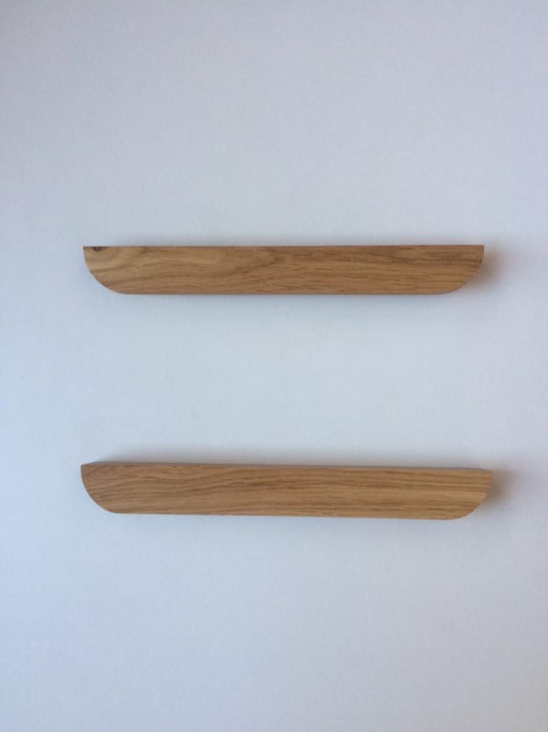 Puede incluir: Dos estantes flotantes de madera con acabado natural montados en una pared blanca. Cada estante es rectangular con un borde curvo en un lado. Los estantes son de madera marr&oacute;n claro y est&aacute;n alineados horizontalmente.