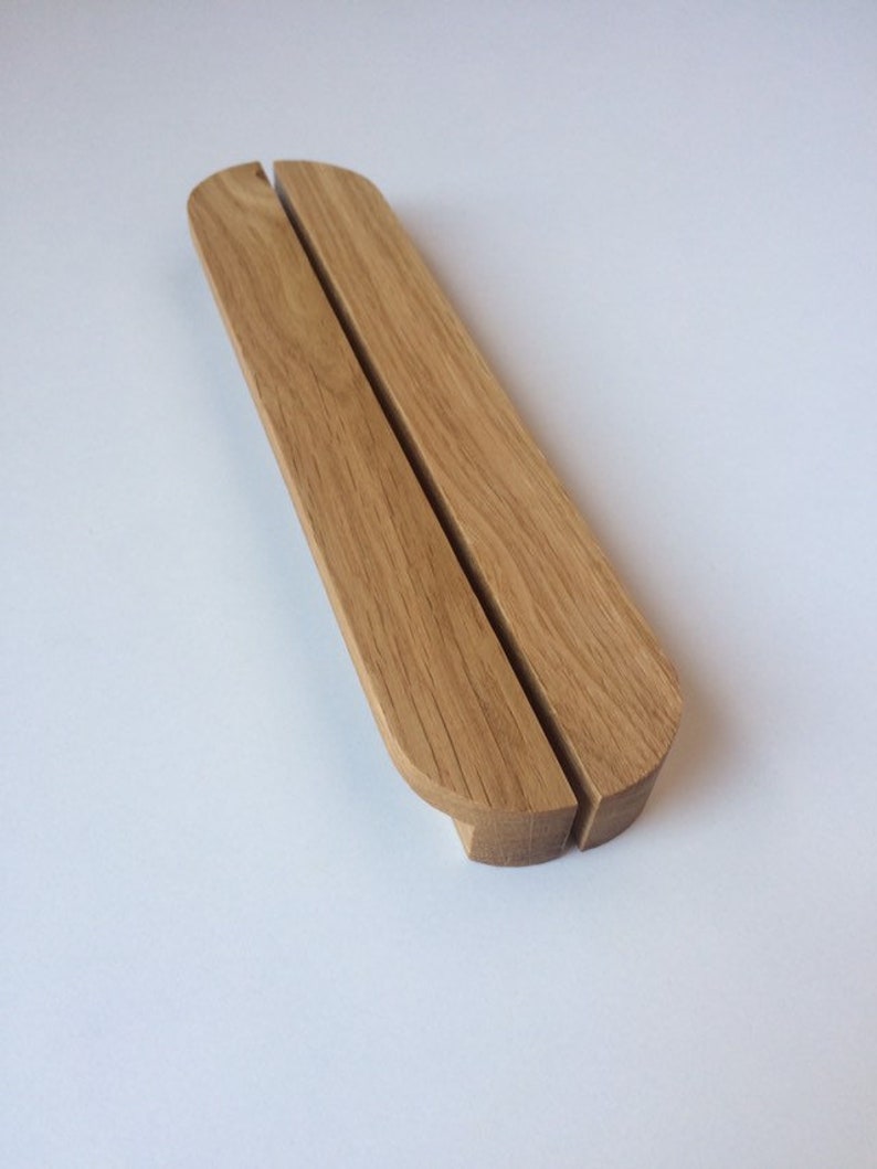 Puede incluir: Un soporte de tel&eacute;fono de madera marr&oacute;n claro con un dise&ntilde;o redondeado. El soporte est&aacute; hecho de dos piezas de madera conectadas, con una ranura en el medio para sostener un tel&eacute;fono. El soporte mide aproximadamente 18 cm de largo.