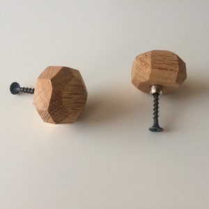 Può includere: Due pomelli per mobili in legno con un design sfaccettato. I pomelli sono realizzati in legno chiaro e hanno una forma geometrica. Ogni pomello ha una vite grigio scuro per l'installazione. I pomelli sono progettati per mobili.