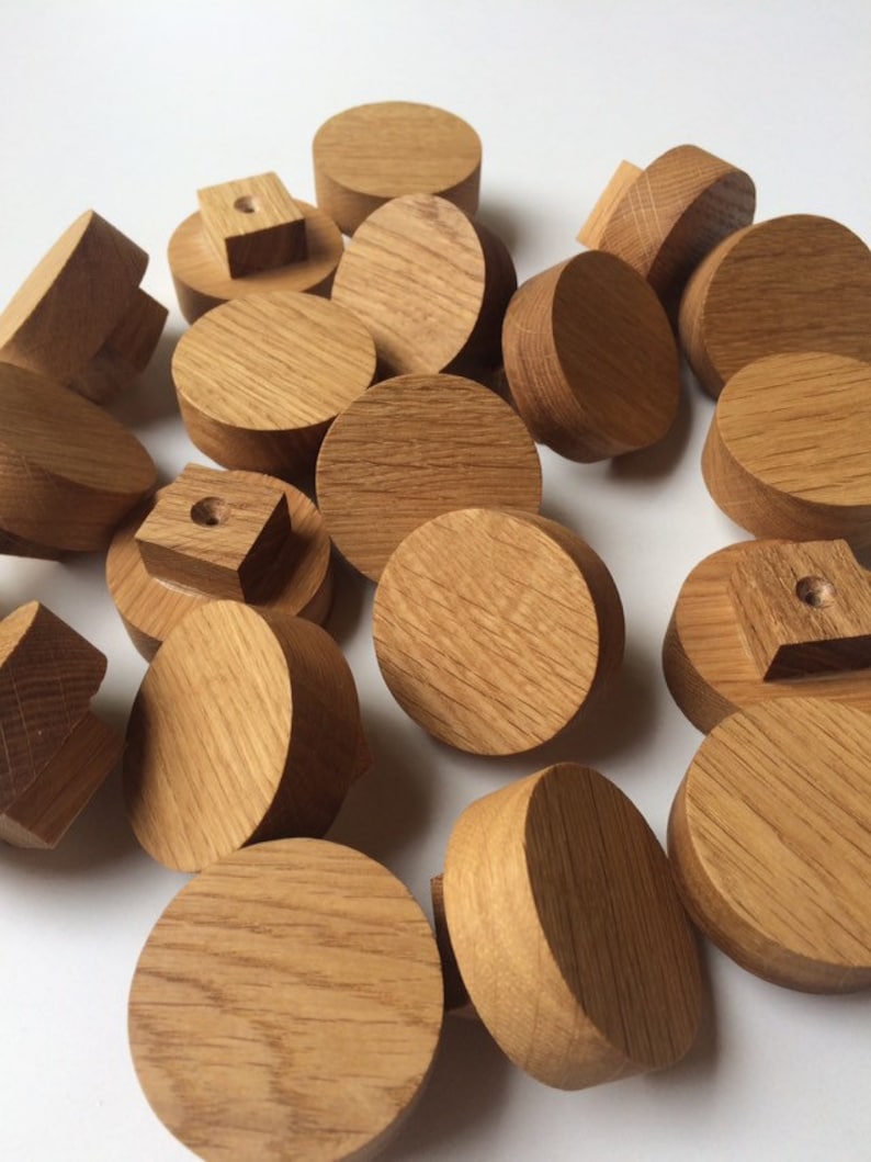 Puede incluir: Una colecci&oacute;n de pomos y tapones de madera sin terminar, de color marr&oacute;n claro. Las formas var&iacute;an, incluyendo formas redondas, cuadradas y cil&iacute;ndricas. La veta de la madera es visible. Estos componentes parecen ser para muebles o proyectos de artesan&iacute;a. Medidas en cent&iacute;metros.