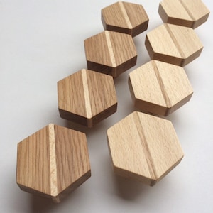 Può includere: Una collezione di otto pomelli esagonali in legno. I pomelli sono realizzati in legno chiaro e scuro, con un dettaglio di scanalatura verticale. I pomelli sono disposti su una superficie bianca.