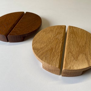 Può includere: Due sottobicchieri in legno, ciascuno composto da due pezzi semicircolari. Uno è marrone scuro, l'altro color rovere chiaro. I sottobicchieri hanno una base piatta e una parte superiore curva.