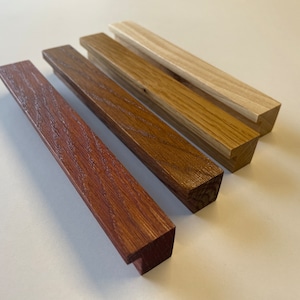 Può includere: Quattro pezzi di legno in varie tonalità di marrone, dal marrone rossiccio al rovere chiaro. Ogni pezzo ha una forma rettangolare con un'estremità leggermente angolata. La venatura del legno è visibile.