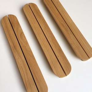 Puede incluir: Tres objetos rectangulares de madera clara, con extremos redondeados y una ranura central. Los objetos est&aacute;n dispuestos diagonalmente sobre una superficie blanca. Se aprecia la veta de la madera.