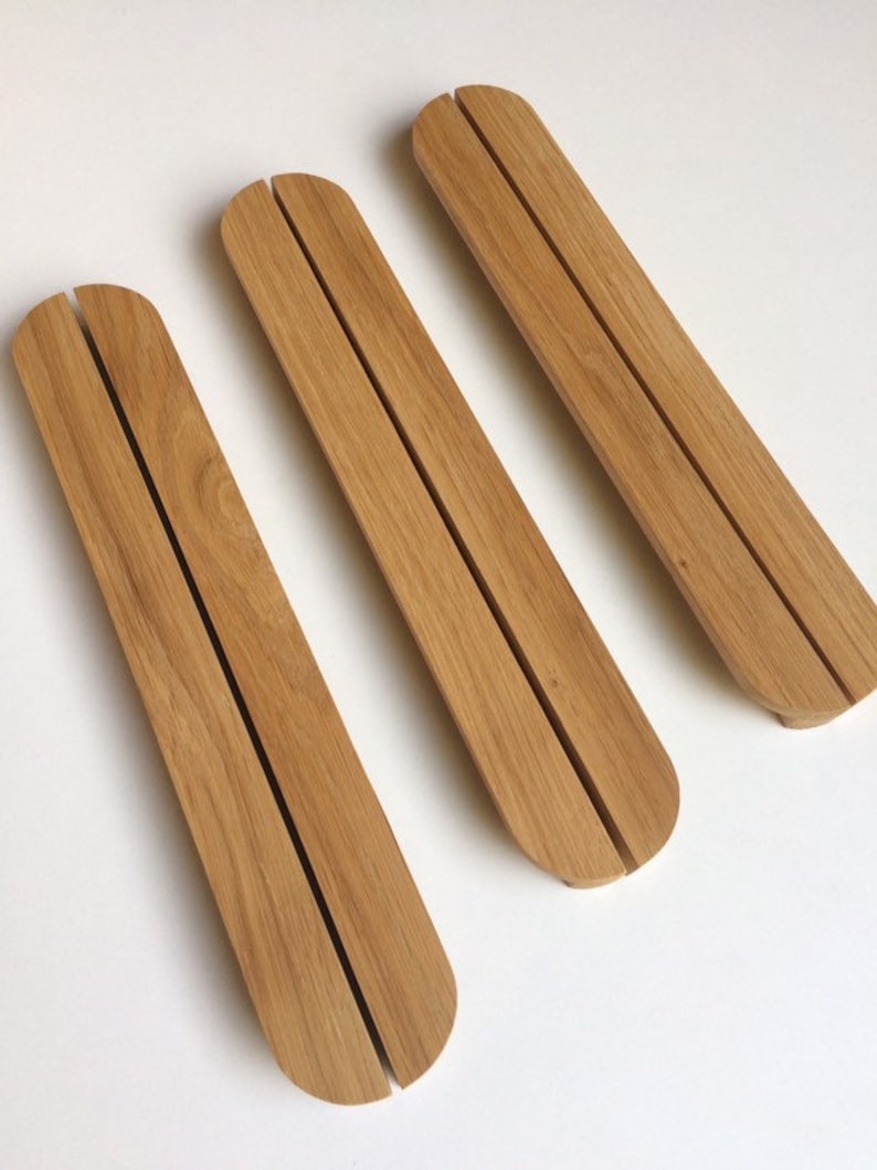 Puede incluir: Tres objetos rectangulares de madera clara, con extremos redondeados y una ranura central. Los objetos est&aacute;n dispuestos diagonalmente sobre una superficie blanca. Se aprecia la veta de la madera.