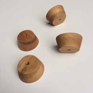 Op de afbeelding: Vier kleine, onafgewerkte houten objecten met een conische vorm en een gat in het midden. De objecten zijn lichtbruin en lijken van hardhout te zijn. Ze zijn gerangschikt op een wit oppervlak.