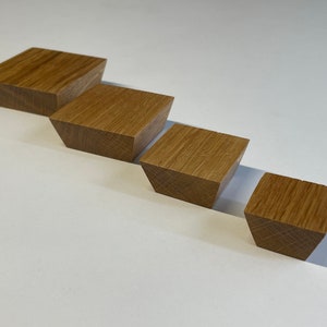 May include: Four wooden blocks of varying sizes are arranged in a diagonal line. Each block is a light brown color with visible wood grain. The blocks have a trapezoidal shape, with the top surface wider than the bottom.