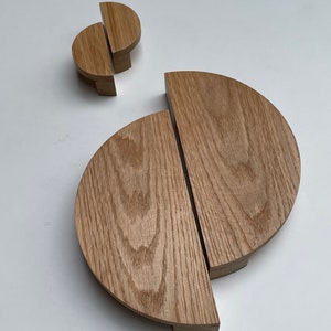 Pode incluir: Dois conjuntos de puxadores de armário de madeira. O conjunto maior é um semicírculo dividido em duas partes. O conjunto menor tem um design semelhante. A madeira tem um grão natural e uma cor castanha clara.