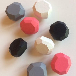 Può includere: Una collezione di nove forme geometriche in legno di vari colori, tra cui grigio, bianco, nero e rosa. Le forme hanno un design sfaccettato e sono disposte su una superficie bianca. Questi oggetti decorativi potrebbero essere usati come giocattoli o per l'arredamento.