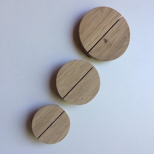 Può includere: Tre sottobicchieri circolari in legno chiaro, ciascuno con una fessura diagonale. Sono disposti in ordine decrescente di dimensioni. Lo sfondo è una superficie bianca uniforme.