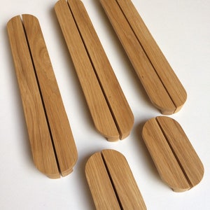 Puede incluir: Un conjunto de cinco soportes de tel&eacute;fono de madera clara. Cada soporte tiene una ranura central para sostener un tel&eacute;fono. Los soportes son de forma ovalada con extremos redondeados, ideales para escritorio.