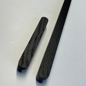 May include: Two black wooden cabinet pulls with a wood grain texture. One is long and rectangular, the other shorter and rounded. Both have a curved end. Ideal for kitchen or bathroom cabinets.