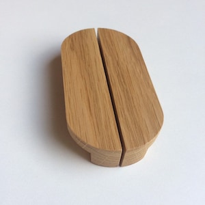 Puede incluir: Un organizador de escritorio de madera con acabado natural. El organizador está hecho de dos piezas de madera conectadas, cada una con una parte superior redondeada y una base plana. La veta de la madera es visible. Para guardar bolígrafos o papeles pequeños.