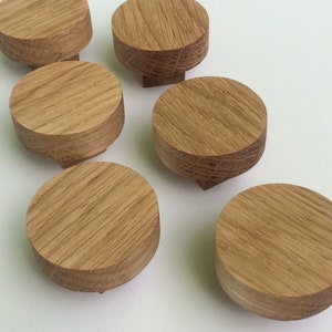 Puede incluir: Seis peque&ntilde;os pomos redondos de madera con un patr&oacute;n de vetas naturales. Los pomos son de color marr&oacute;n claro y tienen una parte superior plana con una base ligeramente c&oacute;nica. Est&aacute;n dispuestos sobre una superficie blanca.