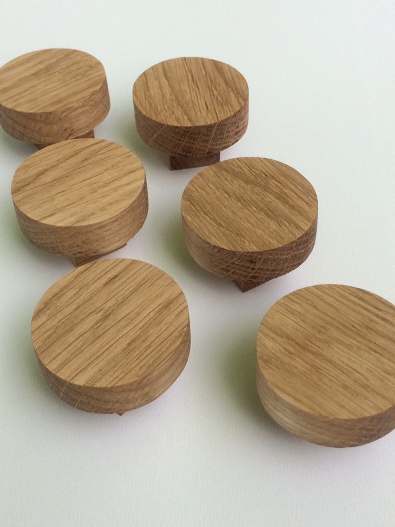 Puede incluir: Seis peque&ntilde;os pomos redondos de madera con un patr&oacute;n de vetas naturales. Los pomos son de color marr&oacute;n claro y tienen una parte superior plana con una base ligeramente c&oacute;nica. Est&aacute;n dispuestos sobre una superficie blanca.