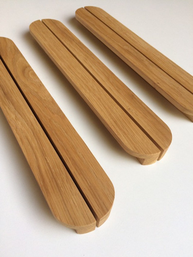 Puede incluir: Tres sujetalibros de madera marr&oacute;n claro, con forma curvada y una ranura central. Los sujetalibros tienen un acabado liso y est&aacute;n dispuestos en diagonal sobre una superficie blanca.