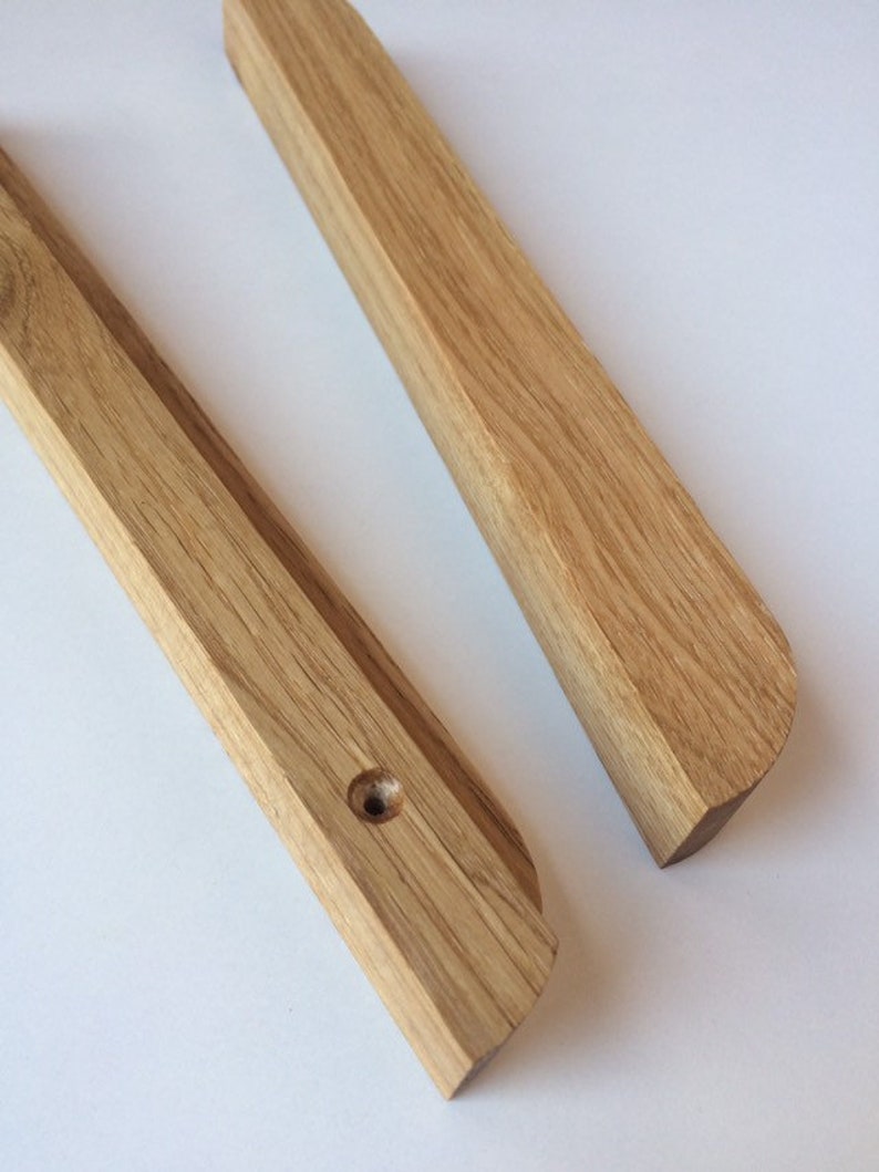 Puede incluir: Dos barras de madera de color marr&oacute;n claro, una con un agujero perforado. Las barras tienen un borde biselado y un extremo redondeado. La veta de la madera es visible. Probablemente son componentes de un art&iacute;culo m&aacute;s grande.