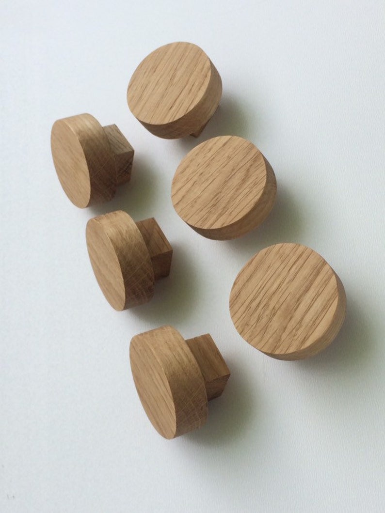 Puede incluir: Seis pomos de madera para muebles. Los pomos son de madera clara y tienen una parte superior redonda y plana con una base cuadrada. La veta de la madera es visible en la superficie. Est&aacute;n dispuestos sobre un fondo blanco.