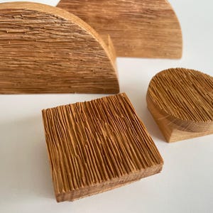 Könnte beinhalten: Vier Holzobjekte mit natürlicher Holzmaserung. Die Formen umfassen einen Halbkreis, ein Quadrat und einen abgerundeten Zylinder. Die Objekte sind auf einer weißen Oberfläche angeordnet und zeigen die Textur und Farbvariationen des Holzes.